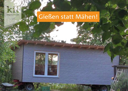 Hellblauer Bauwagen in grüner, bewachsener Umgebung