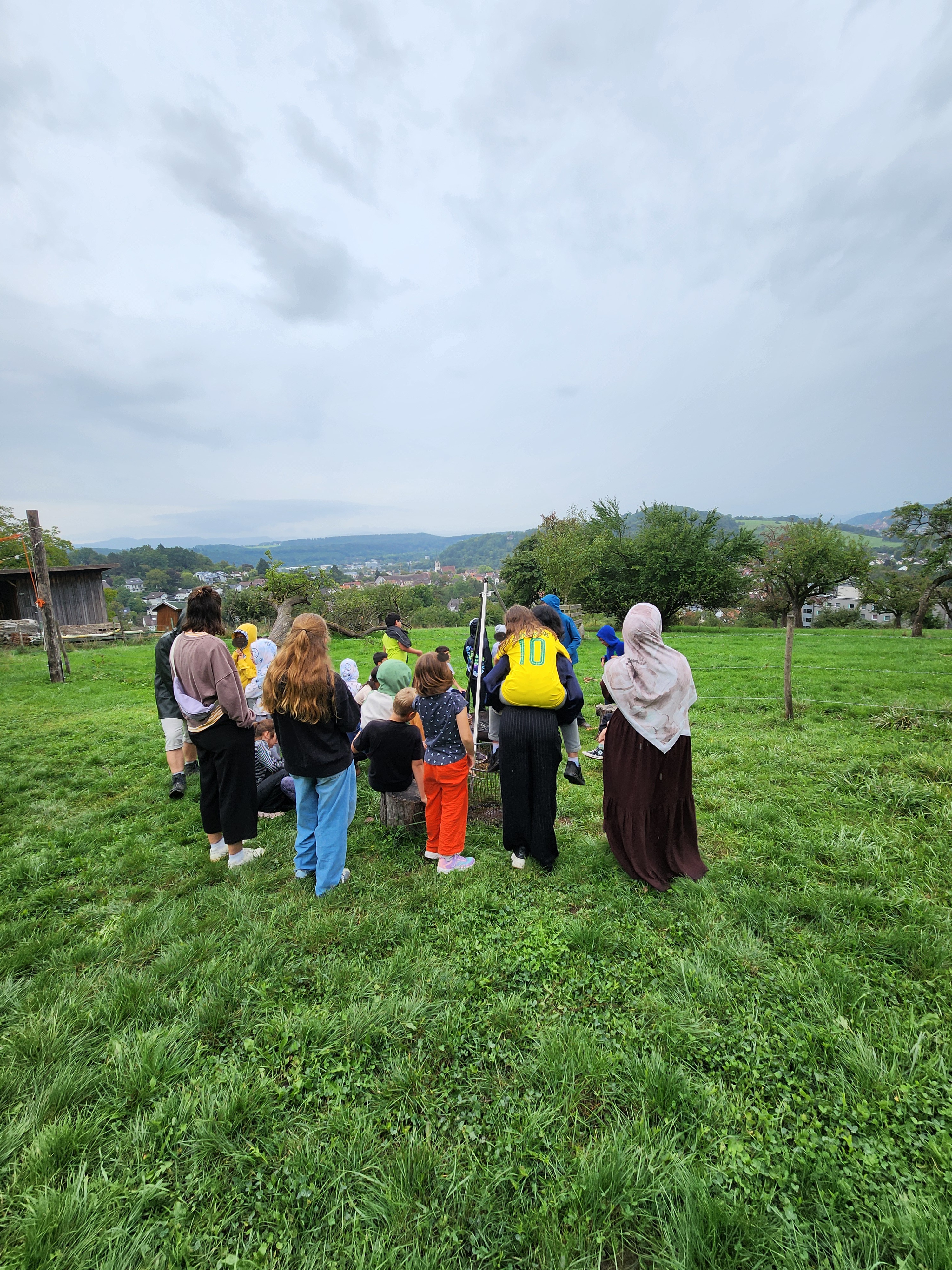Gruppe von Kindern und Betreuern auf einem Feld, mit dem Rücken zum Betrachter stehend